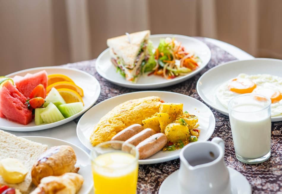A breakfast spread featuring omelet, sausages, fruit, salad, toast, and drinks.