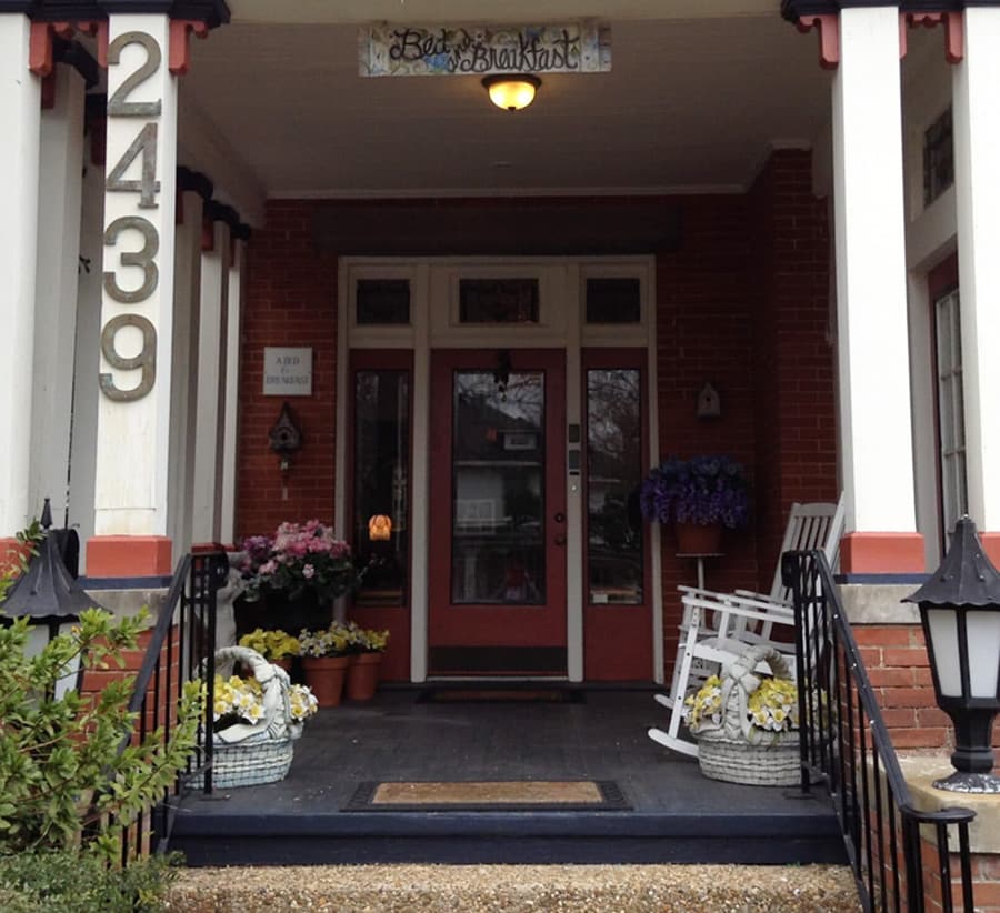 A cozy bed and breakfast entrance with a welcoming porch, flower baskets, and a rocking chair.