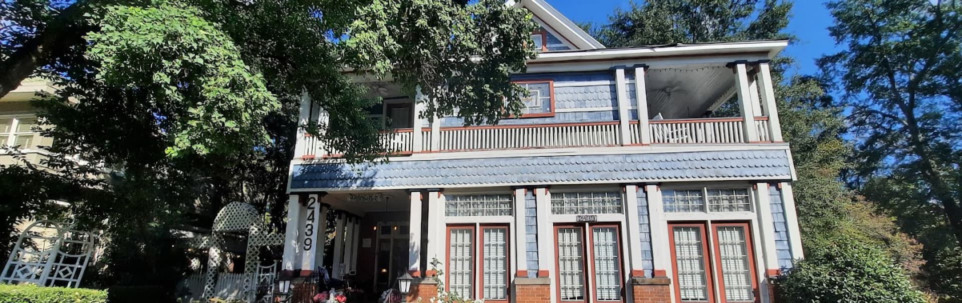 A large, vintage two-story house with a covered porch surrounded by greenery.