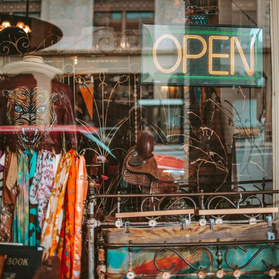 A vintage shop window displaying colorful clothing and accessories, with a bright "OPEN" sign.