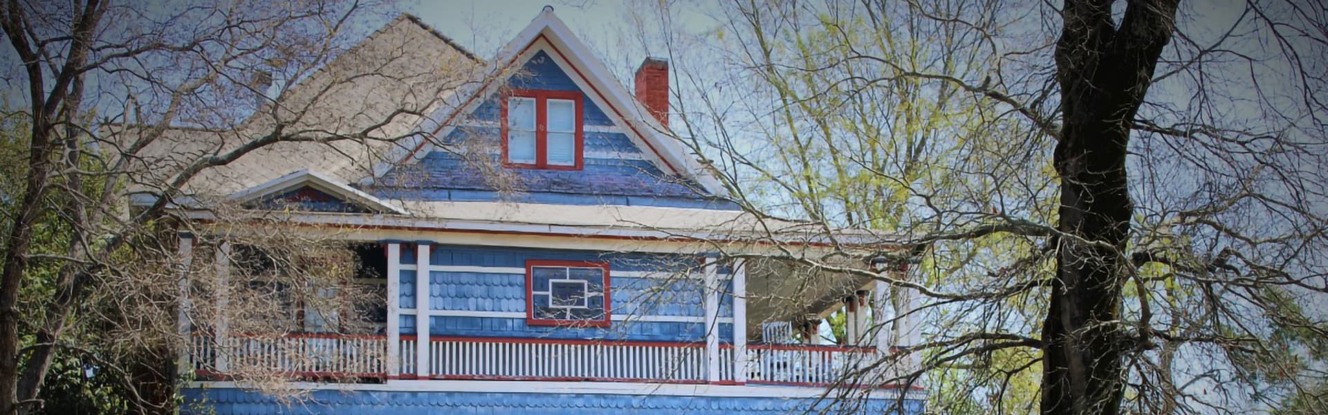 A blue, two-story house with a porch and red accents is surrounded by bare trees.