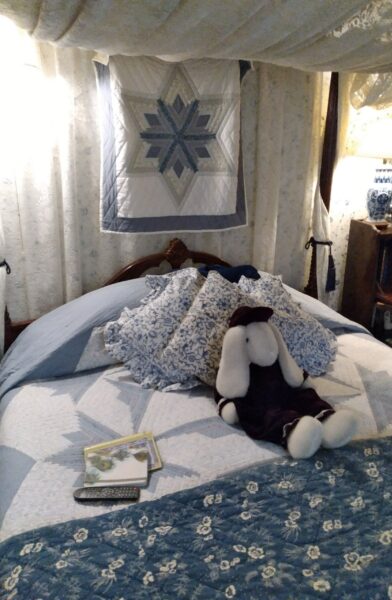 A cozy bed adorned with blue floral quilts and decorative pillows, accompanied by a stuffed bunny and open books.