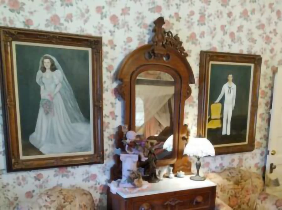 A vintage living room featuring two portraits, a mirror, and floral wallpaper.