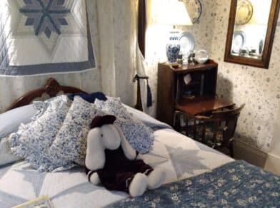 A cozy bedroom featuring a bed with patterned pillows, a stuffed bunny, and vintage decor.