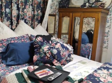 A cozy bedroom featuring floral-patterned bedding, curtains, and a wooden wardrobe.