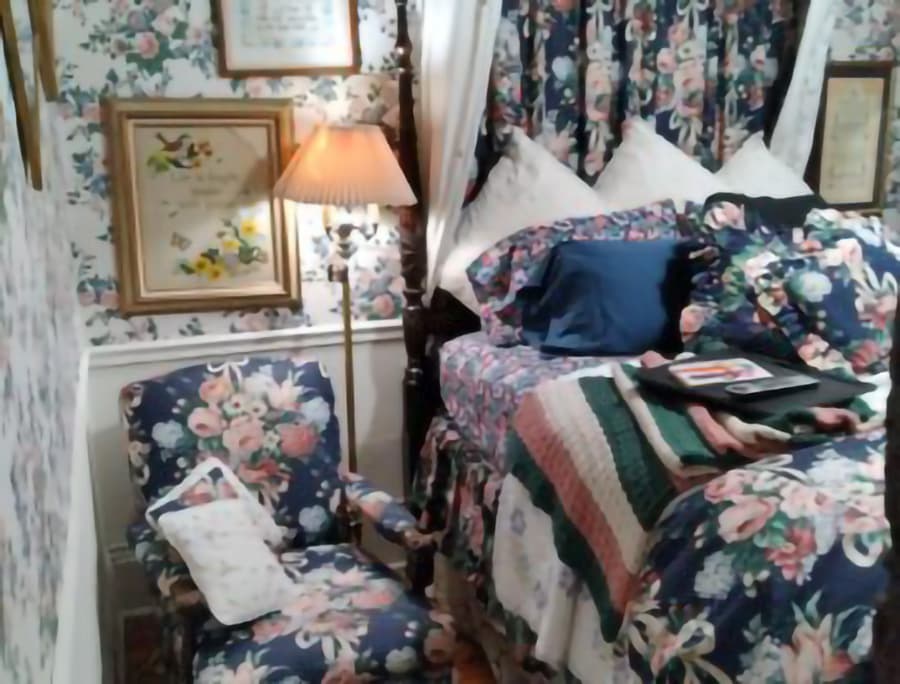 A cozy bedroom featuring floral wallpaper, a bed with patterned bedding, and a matching armchair.