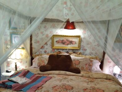 A cozy, floral-decorated bedroom featuring a canopy bed, soft lighting, and a plush bear-shaped pillow.